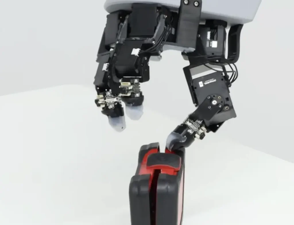 Close-up of a black-and-gray robotic arm gripping a red-and-black object, highlighting precision machinery in a clean, futuristic setting.