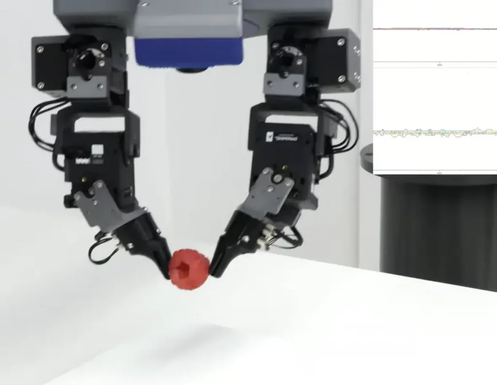 A dual-arm robotic gripper carefully holds a red spherical object above a white surface in a clean laboratory, conveying precision.